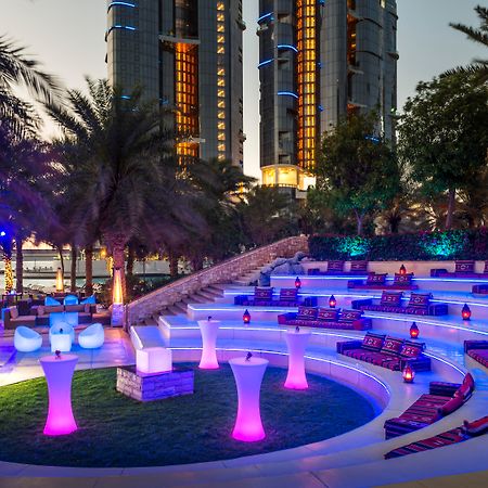 Sheraton Abu Dhabi Hotel&Resort Esterno foto The photo shows an upscale outdoor lounge area, likely at a hotel or resort. The seating is arranged in a circular amphitheater style, featuring plush cushions in various colors and illuminated with purple lighting. There are small tables and decorat