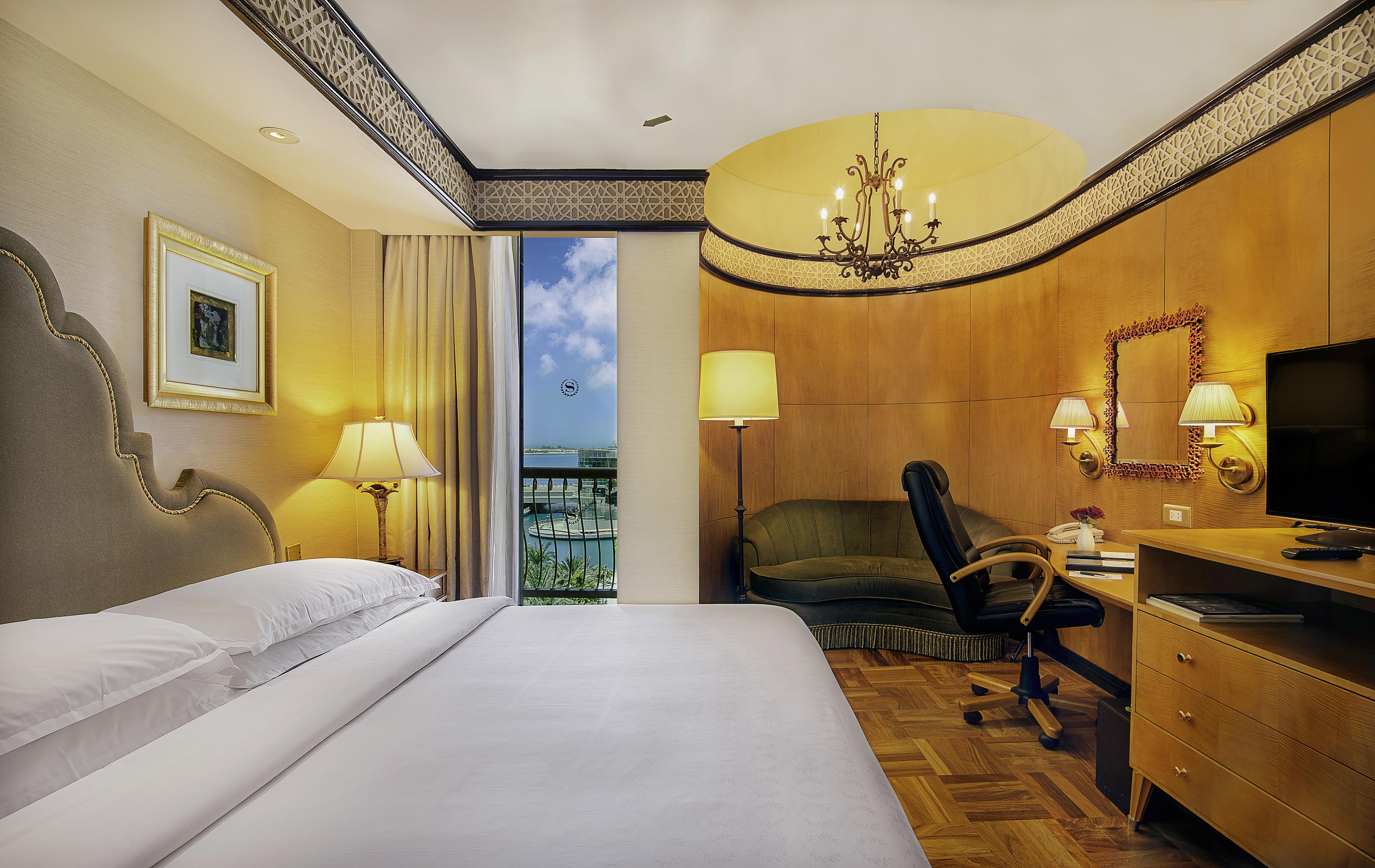 Sheraton Abu Dhabi Hotel&Resort Esterno foto The photo shows a hotel room that features modern and elegant decor. There is a large bed with white linens positioned near the front of the room. On one side of the bed, there are bedside lamps providing a warm glow. 

In the corner, there is a smal