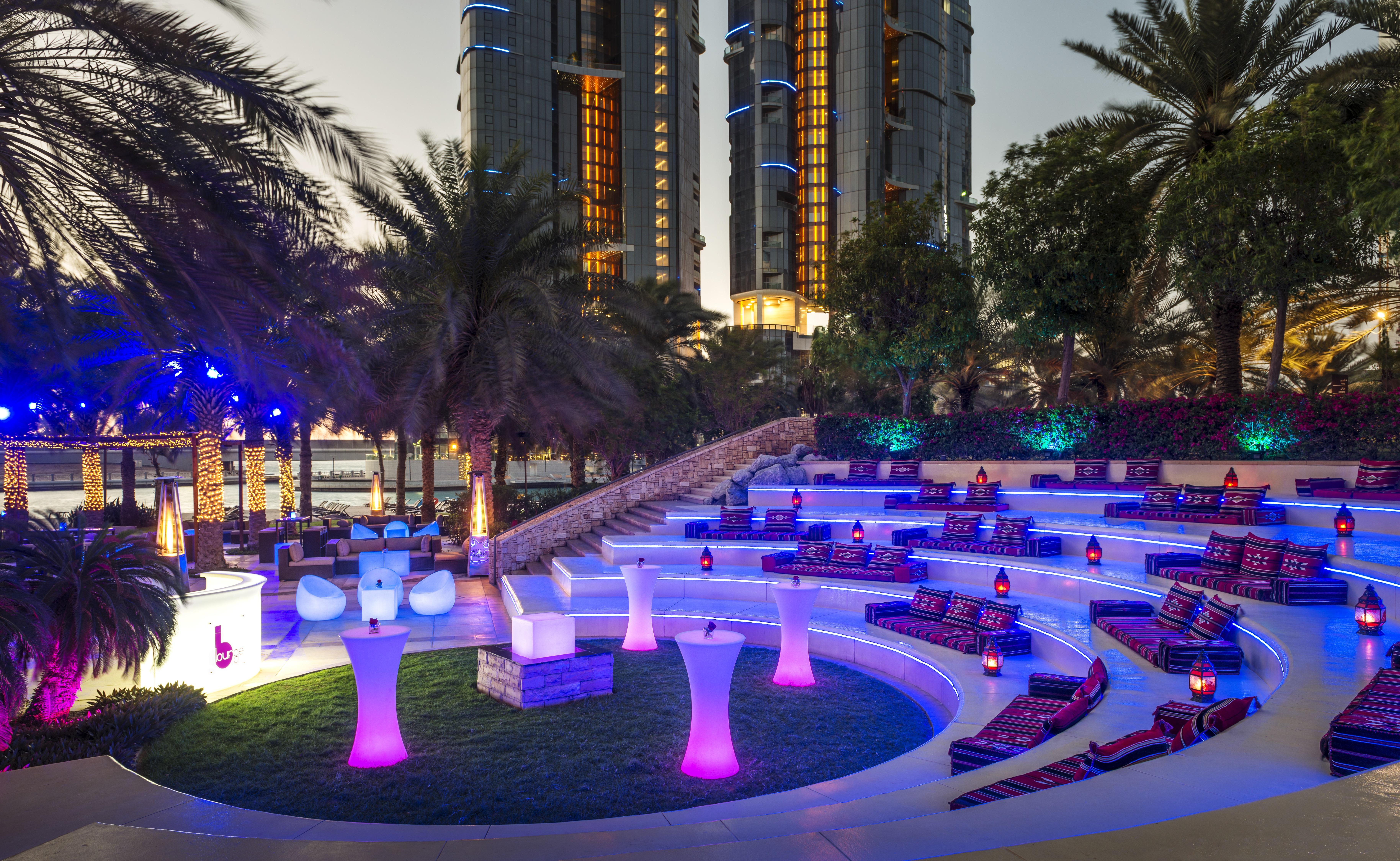 Sheraton Abu Dhabi Hotel&Resort Esterno foto The photo shows an upscale outdoor lounge area, likely at a hotel or resort. The seating is arranged in a circular amphitheater style, featuring plush cushions in various colors and illuminated with purple lighting. There are small tables and decorat