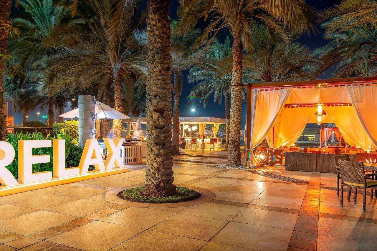 Sheraton Abu Dhabi Hotel&Resort Esterno foto The photo depicts a nighttime scene in a tropical setting, likely a resort or a beachfront area. There are several tall palm trees, creating a lush atmosphere. A prominent feature in the foreground is a large, illuminated sign that reads "RELAX," sug