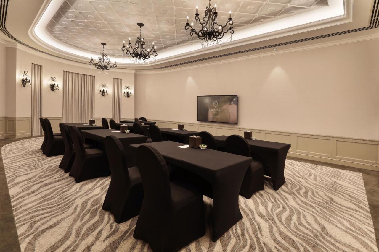 Sheraton Abu Dhabi Hotel&Resort Esterno foto The photo shows a meeting or conference room designed for professional gatherings. It features several long tables arranged with black tablecloths and matching chairs. The room has a sophisticated ambiance, highlighted by decorative chandeliers hangi