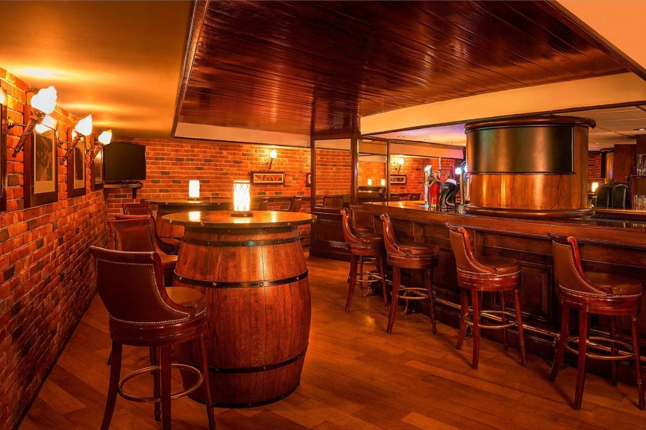 Sheraton Abu Dhabi Hotel&Resort Esterno foto The photo shows a cozy and inviting interior of a bar. The decor features warm wooden tones with brick walls, creating a rustic atmosphere. There is a circular wooden table made from a barrel at the center, surrounded by several high-backed chairs. I