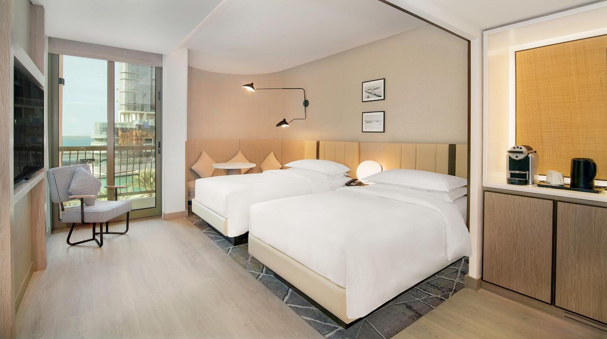 Sheraton Abu Dhabi Hotel&Resort Esterno foto The photo shows an interior view of a modern hotel room. It features two beds with white linens, placed against a light-colored wall. There are decorative items on the wall, including two framed pictures. A sleek bedside lamp is mounted on the wall a