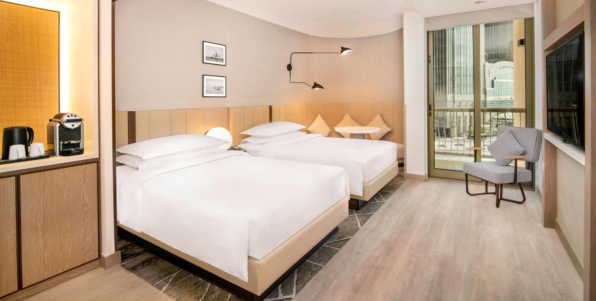 Sheraton Abu Dhabi Hotel&Resort Esterno foto The photo depicts a modern hotel room featuring two neatly made beds with white linens and upholstered headboards. The room has a light, neutral color palette with wooden flooring. On the wall, there are two framed pictures. A stylish wall-mounted la