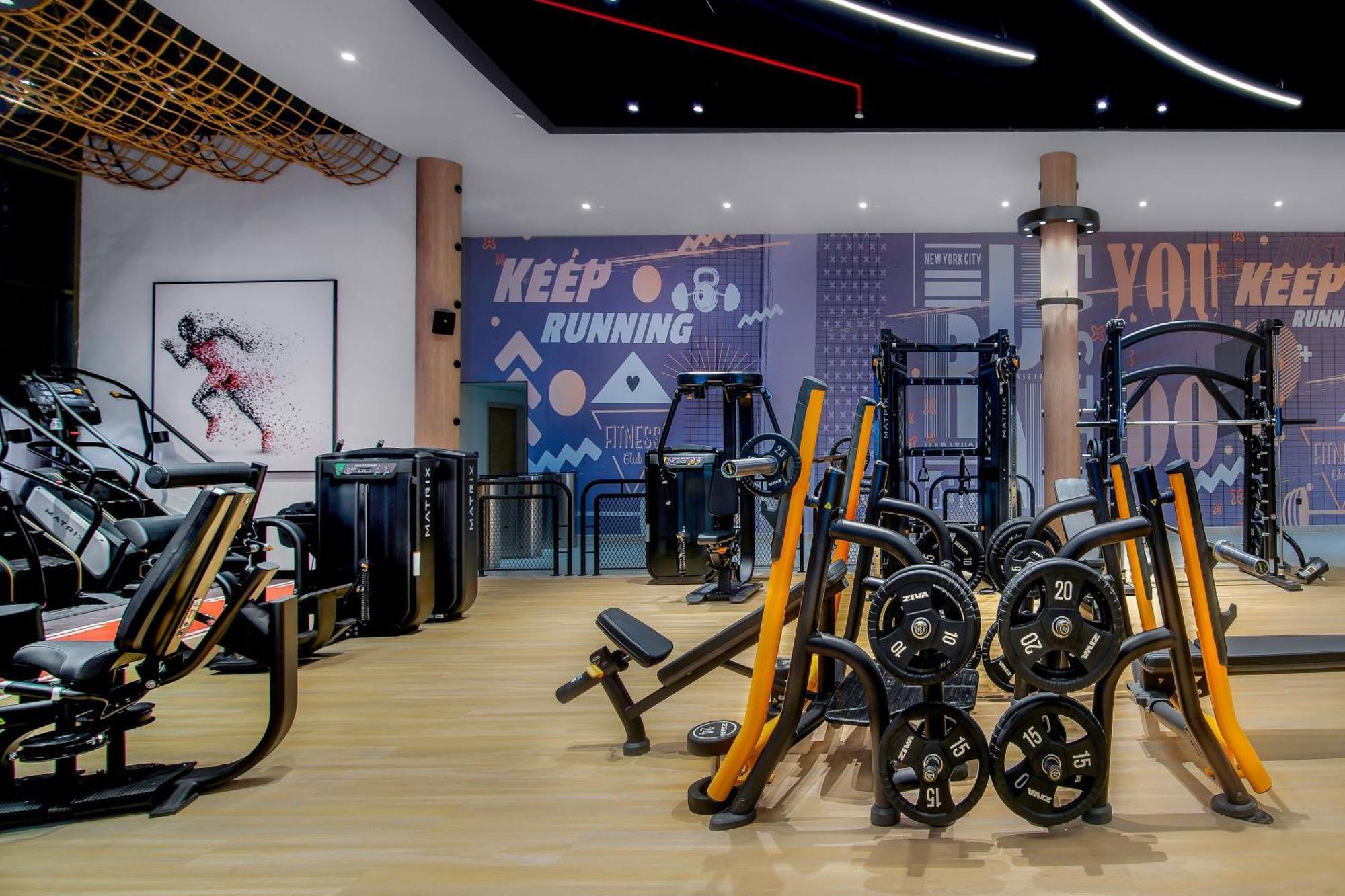 Sheraton Abu Dhabi Hotel&Resort Esterno foto The photo shows a modern gym interior. It features various exercise equipment, including weight machines and free weights, prominently displayed on a wooden floor. The walls are adorned with motivational graphics and designs. A large poster of an ath