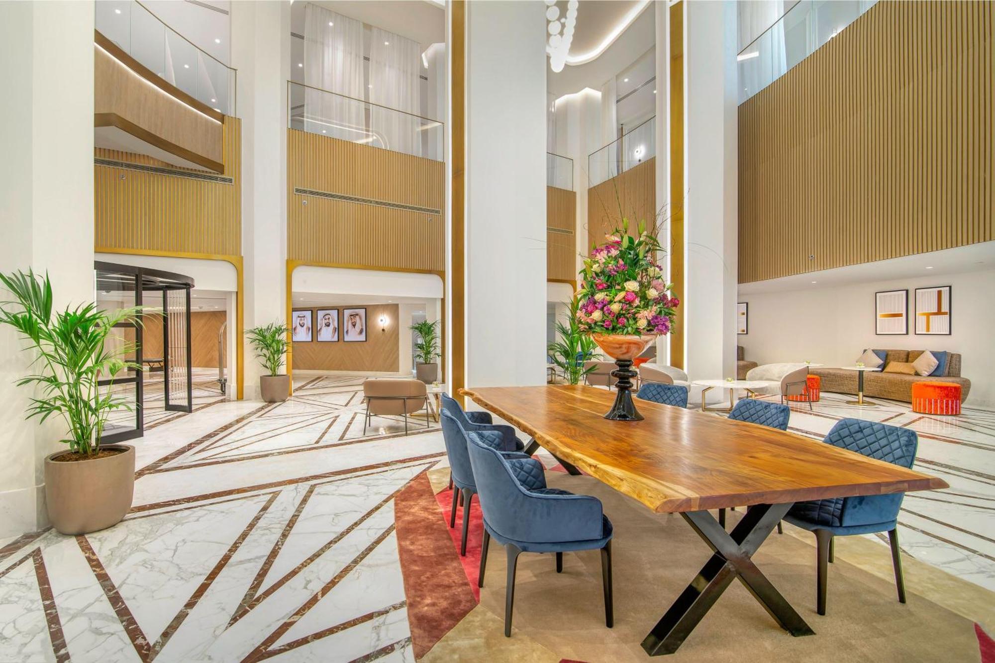 Sheraton Abu Dhabi Hotel&Resort Esterno foto The photo features an elegant lobby or lounge area of a hotel or a similar building. It has a high ceiling with large windows that allow natural light to flood in. A long wooden table with black legs is positioned centrally, surrounded by several blu