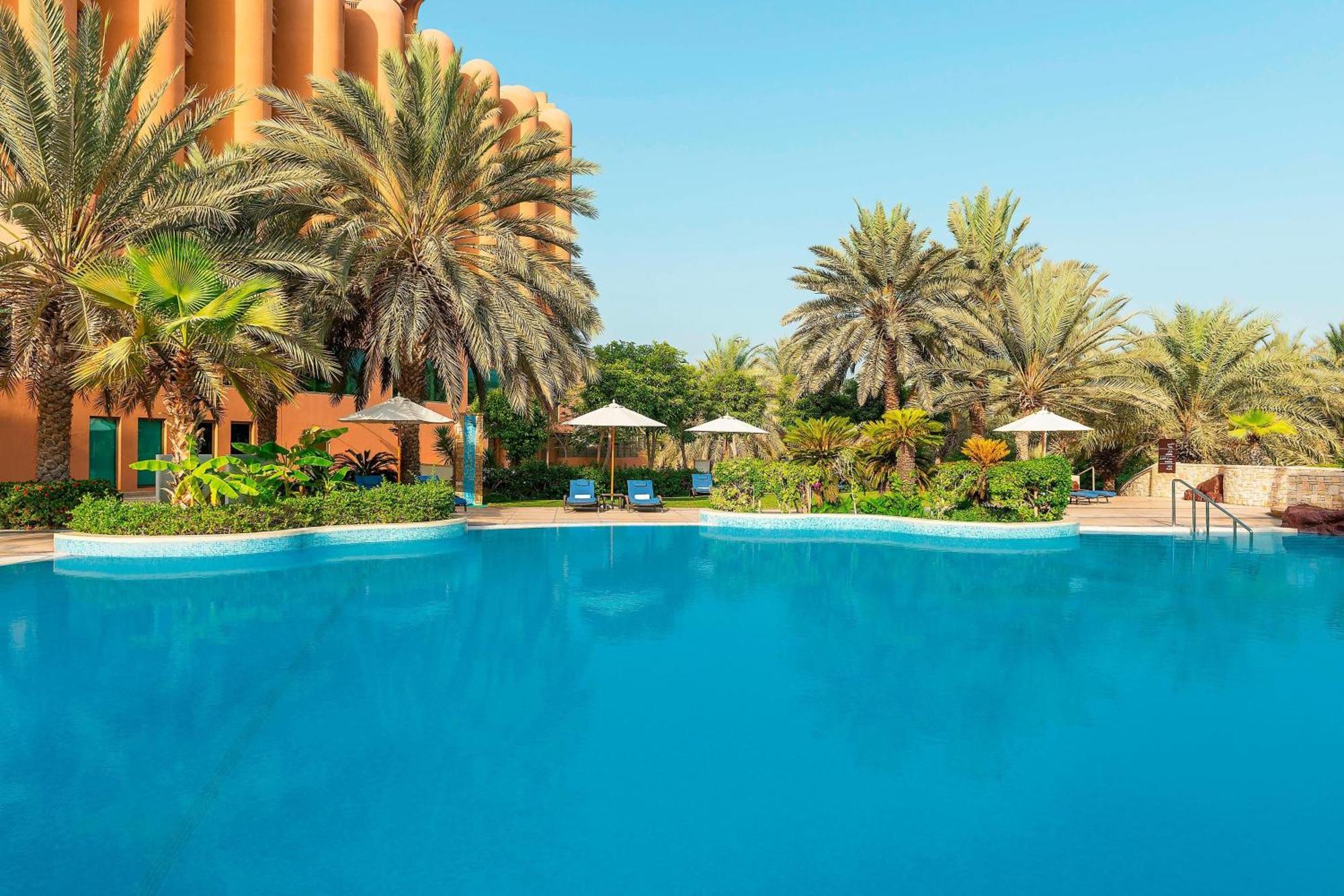 Sheraton Abu Dhabi Hotel&Resort Esterno foto The photo shows a tranquil swimming pool surrounded by lush tropical landscaping. There are tall palm trees and well-kept greenery creating a lush environment. Several lounge chairs are positioned beside the pool, along with sun umbrellas for shade. 