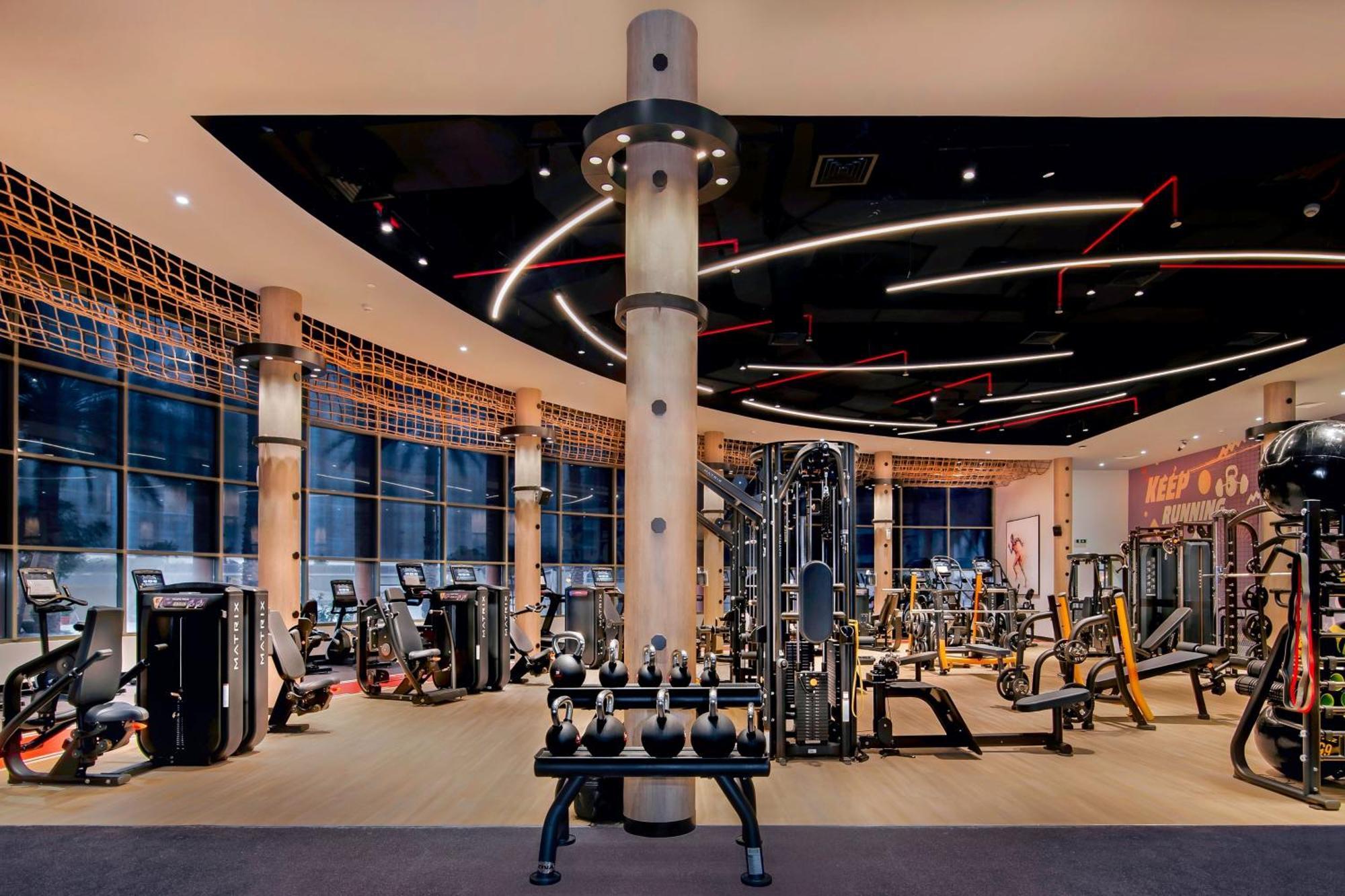 Sheraton Abu Dhabi Hotel&Resort Esterno foto The photo shows a modern gym interior featuring various fitness equipment. There are multiple workout stations, including weight machines and free weights like dumbbells. The design includes large windows that allow natural light to flood the space, 