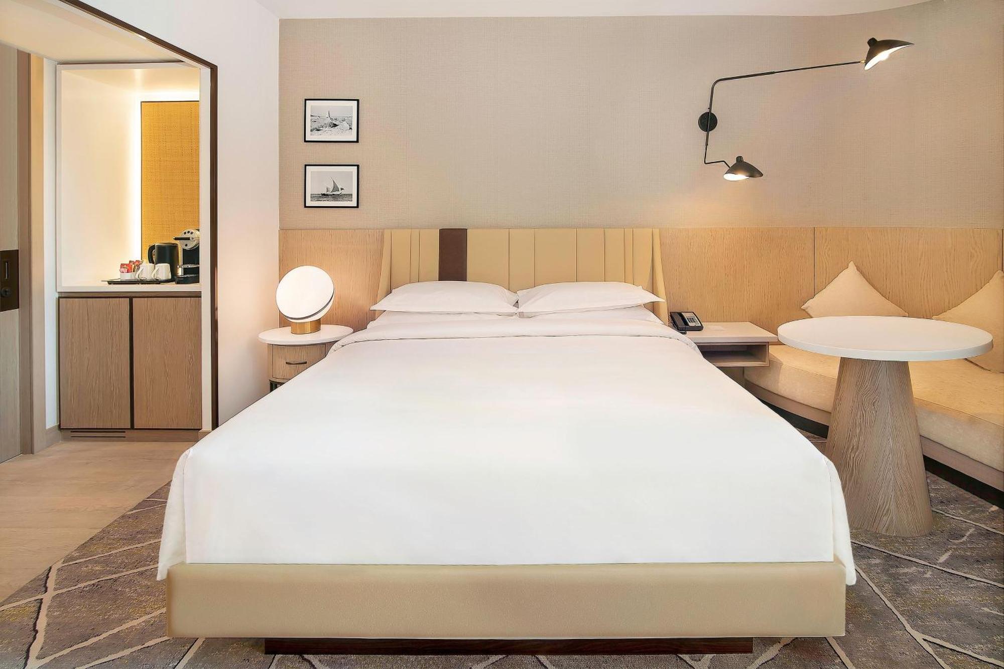 Sheraton Abu Dhabi Hotel&Resort Esterno foto The photo shows a modern hotel room featuring a large bed with crisp white linens placed against a light-colored wall. On either side of the bed, there are bedside lamps, and above the bed, there is a stylish wall-mounted light fixture. The room incl