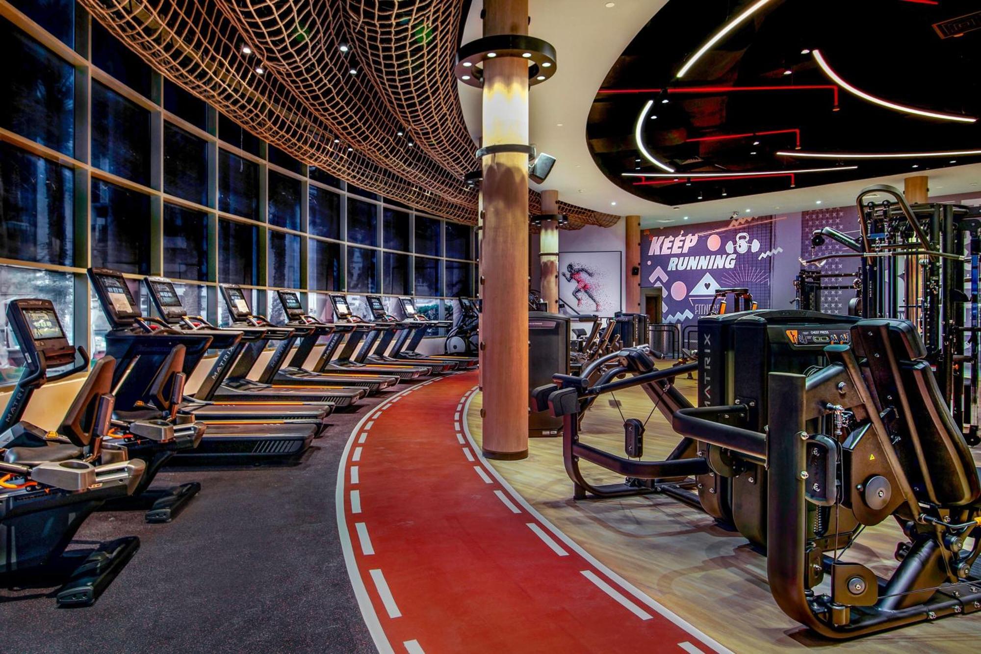 Sheraton Abu Dhabi Hotel&Resort Esterno foto The photo shows a modern gym interior. There are several treadmills lined up against large windows that provide natural light. The floor has a track-like design, painted in red and white, giving a sporty feel. In addition to the treadmills, there are