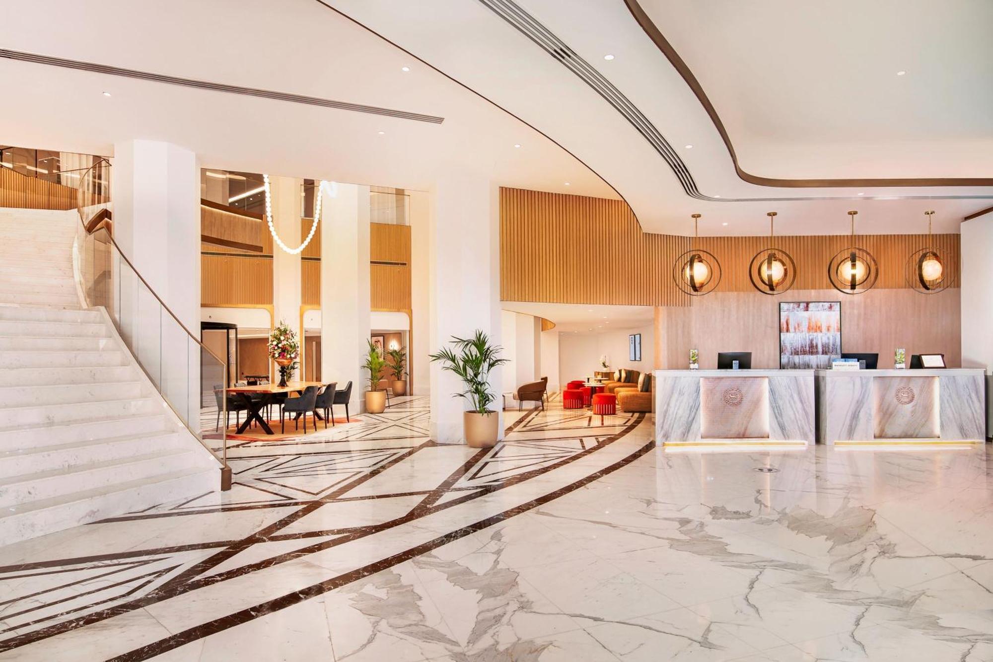 Sheraton Abu Dhabi Hotel&Resort Esterno foto The photo depicts a modern hotel lobby. It features a spacious area with marble flooring and an elegant design. To the left, there is a grand staircase leading to an upper level. The reception desk is prominently placed in the center, with stylish li
