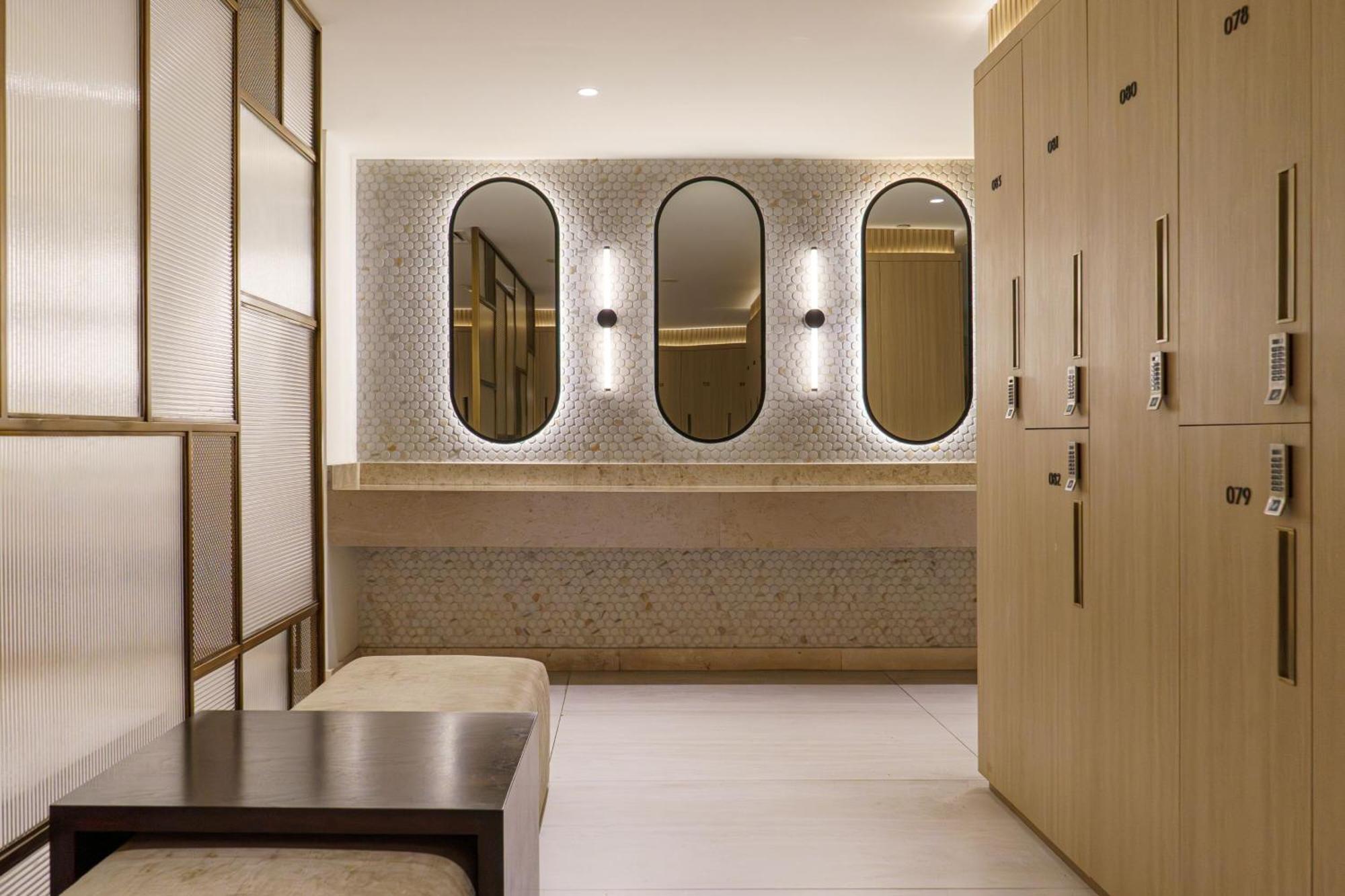Sheraton Abu Dhabi Hotel&Resort Esterno foto The photo shows a modern bathroom or changing area featuring a minimalist design. There are three oval mirrors mounted on a wall, illuminated by built-in lighting. Below the mirrors, there's a countertop made of a light-colored material. On one side,