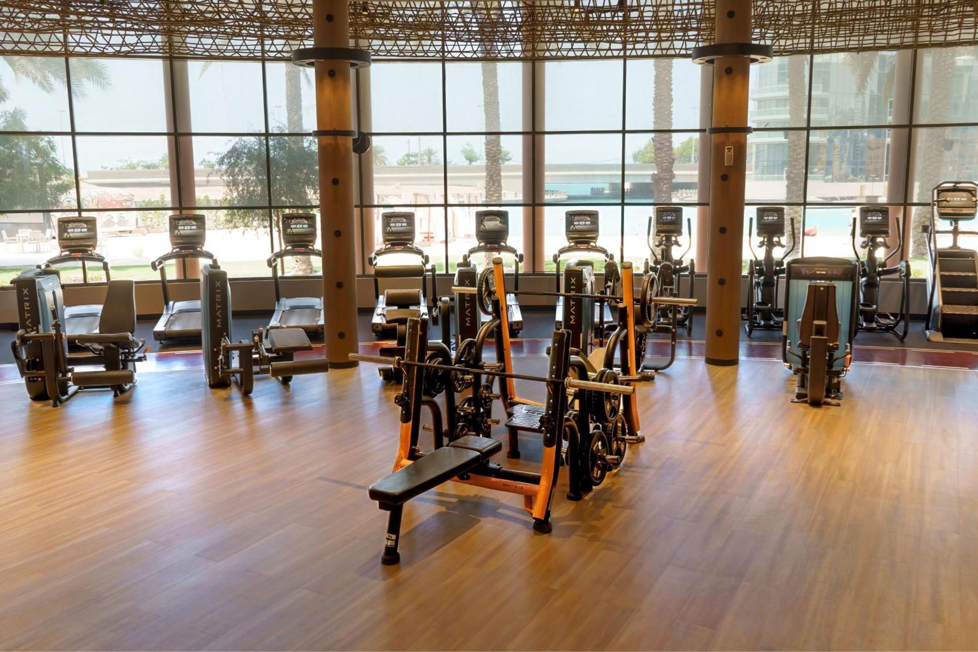 Sheraton Abu Dhabi Hotel&Resort Esterno foto The photo shows a modern gym interior with multiple fitness machines. In the foreground, there is a bench press setup with weights. Surrounding it, there are several cardio machines, such as treadmills and stationary bikes, lined up against large win