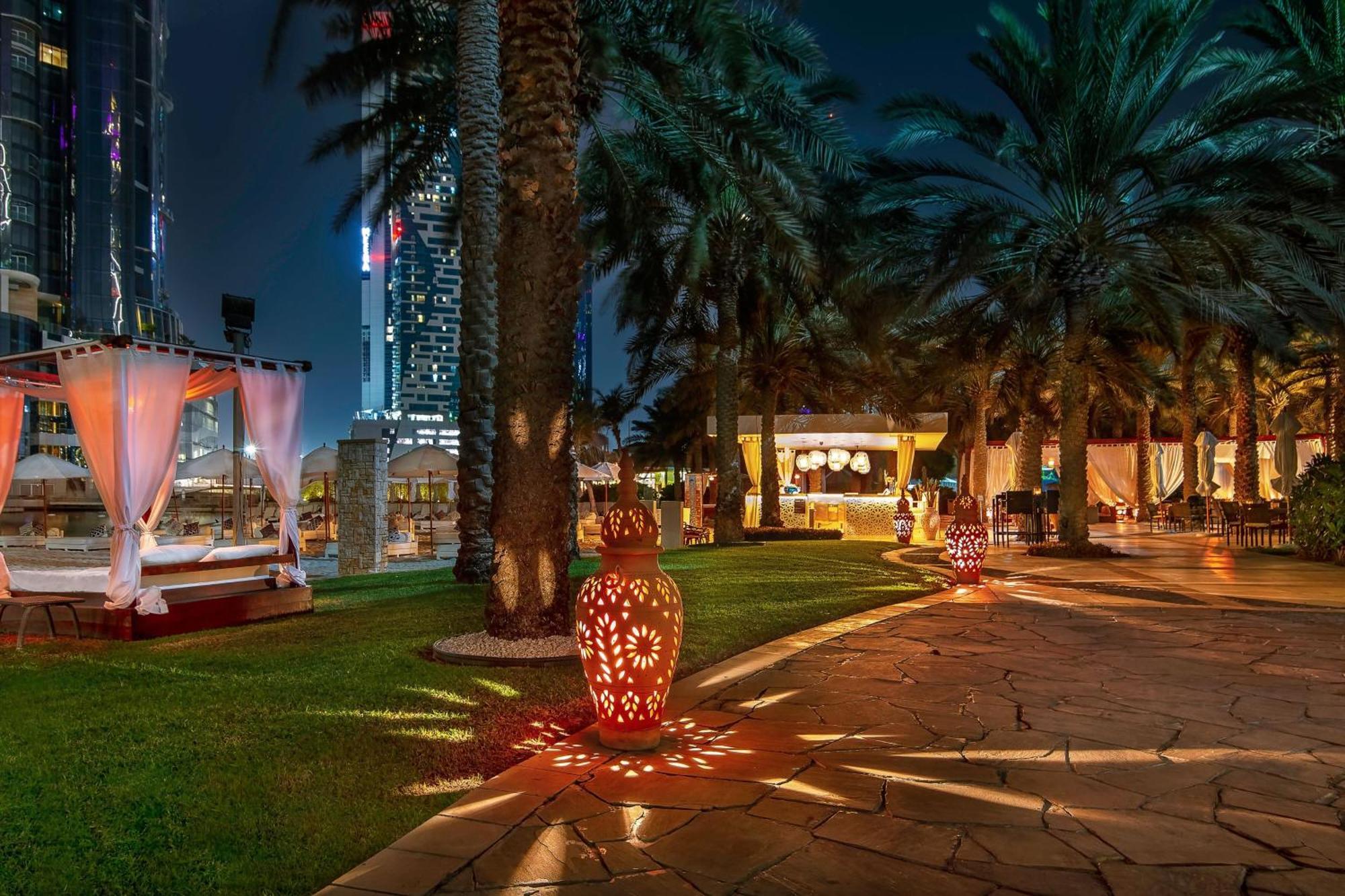 Sheraton Abu Dhabi Hotel&Resort Esterno foto The photo depicts a beautifully designed outdoor area at night, featuring palm trees and a well-maintained grassy pathway. There are decorative lanterns placed along the path, casting warm, intricate patterns on the ground. In the background, there a