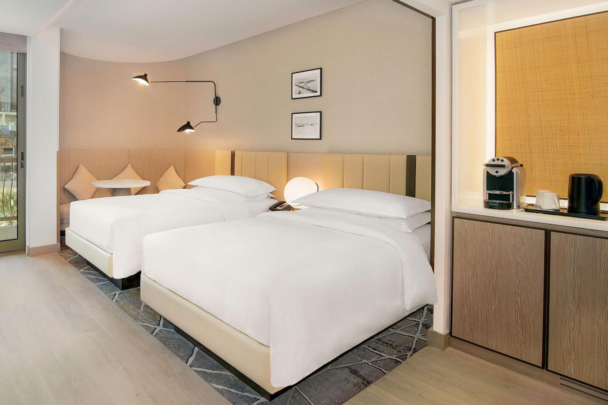 Sheraton Abu Dhabi Hotel&Resort Esterno foto The image shows a modern hotel room featuring two neatly made beds with white bedding. The walls are painted in a light color, and there are decorative elements such as framed pictures on the wall above the beds. A sleek lamp is mounted on the wall b